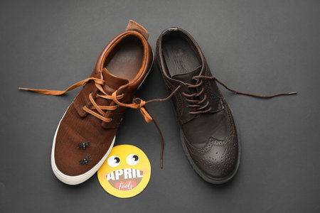 Different shoes with tied laces and fake spiders on dark background. April Fool's Day prank