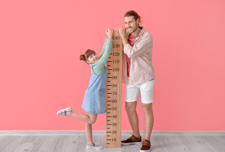 Cute little girl and her father measuring height on color background