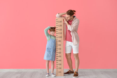 Cute little girl and her father measuring height on color backgroundの写真素材
