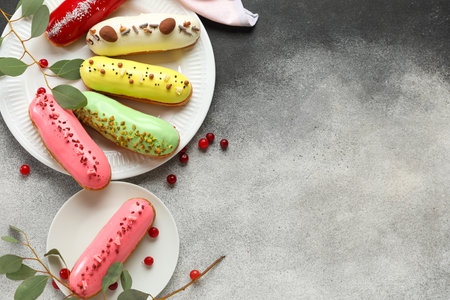Plates with delicious glazed eclairs, eucalyptus and cranberry on gray background