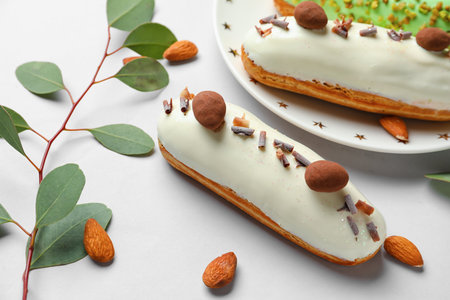 Plate with delicious glazed eclairs, almond nuts and eucalyptus on white backgroundの写真素材