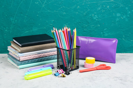 Holder with stationery, notebooks and pencil case on table near blackboardの写真素材