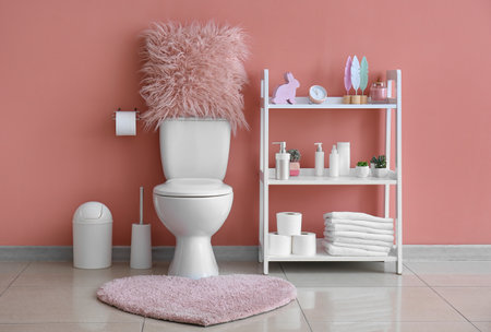 Interior of restroom with ceramic toilet bowl, rug and shelving unit near pink wallの写真素材