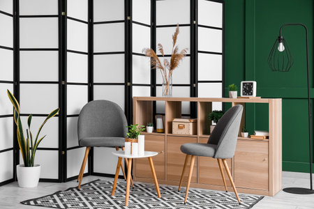 Interior of living room with folding screen, chairs and end table near green wallの写真素材