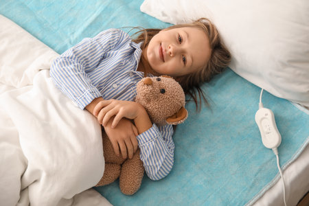 Little girl with toy lying on electric heating pad in bedroomの写真素材