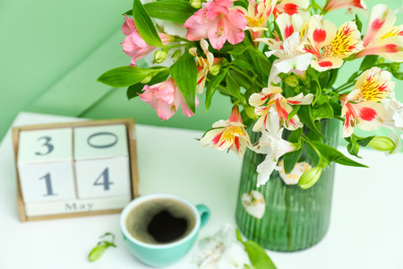Vase with beautiful alstroemeria flowers, cup of coffee and cube calendar on table near color wall, closeup. mother's day celebrationの写真素材