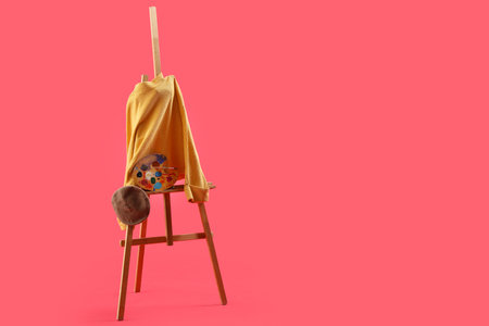 Easel with yellow sweater, beret and paint palette on red backgroundの写真素材