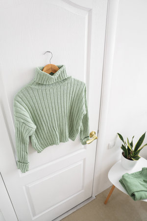 Green sweater hanging on white door in room