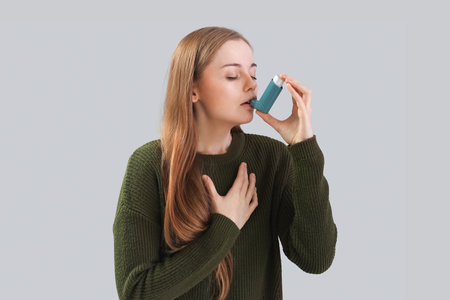 Young woman with inhaler on gray backgroundの写真素材