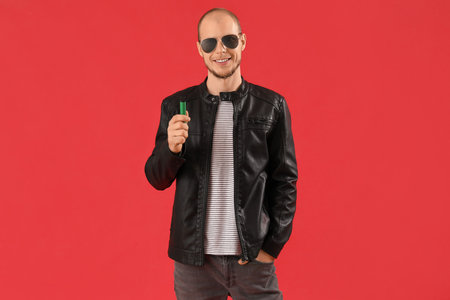 Young man in sunglasses with disposable electronic cigarette on red background