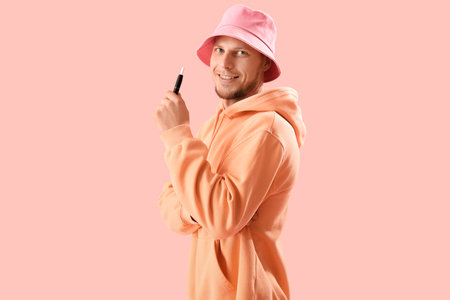 Young man in bucket hat with disposable electronic cigarette on pink backgroundの写真素材