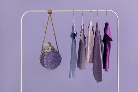 Rack with stylish clothes and bag near lilac wallの写真素材