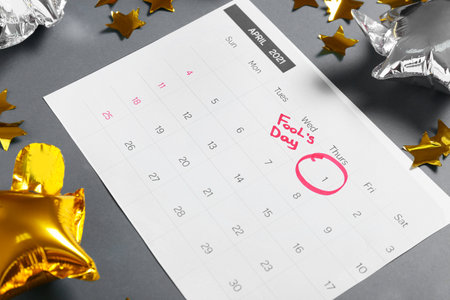 Calendar with marked date of April Fool's Day and party decor on gray background