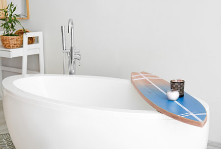 Bathtub with surfboard and aroma candles in modern interior of bathroomの写真素材