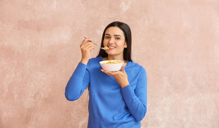 Beautiful young woman eating cornflakes on color background