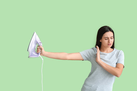 Beautiful young woman with iron on color backgroundの写真素材