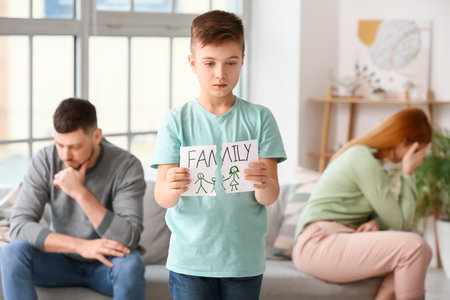 Sad little boy with torn drawing of family after quarrel between his parents at homeの写真素材