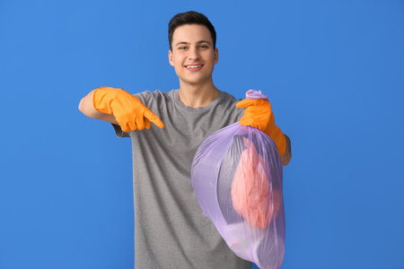 Young man with garbage bag on color backgroundの写真素材