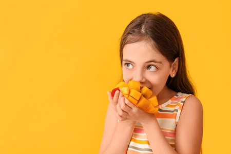 Cute little girl eating tasty mango on color backgroundの写真素材