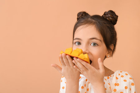 Cute little girl eating tasty mango on color backgroundの写真素材