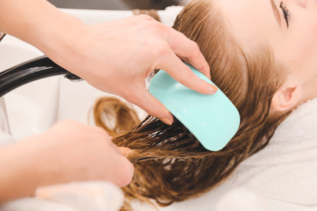 Female hairdresser combing wet hair of client in beauty salon, closeup