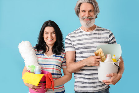 Mature couple with cleaning supplies on color backgroundの写真素材