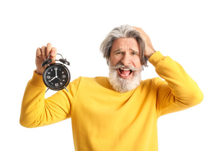 Displeased senior man with alarm clock on white backgroundの写真素材