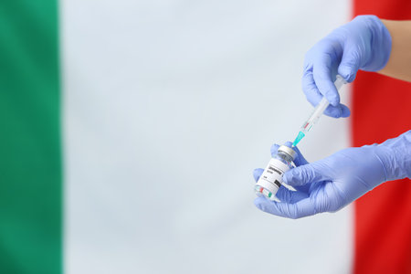 Doctor's hand with COVID-19 vaccine against flag of Italyの写真素材