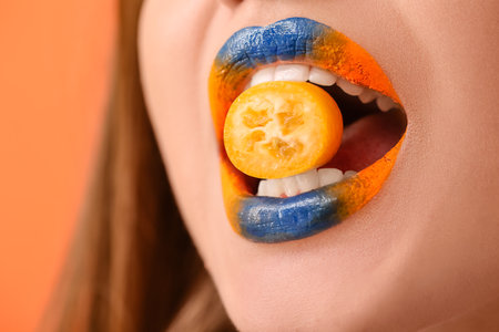 Beautiful young woman with creative makeup and cumquat, closeupの写真素材