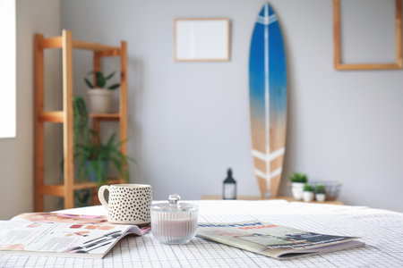 Cup with magazines and aroma candles on dining table