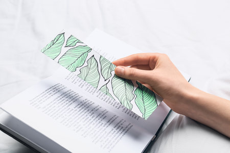Woman with cute bookmark and book on bedの写真素材