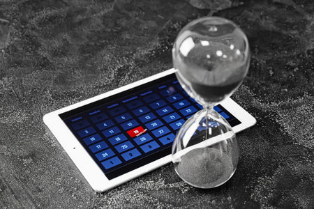 Tablet computer and hour glass on dark background. Dead line conceptの写真素材