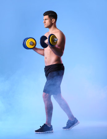 Sporty young man training with dumbbells on color backgroundの写真素材