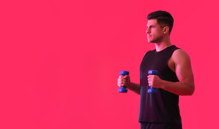Sporty young man training with dumbbells on color backgroundの写真素材
