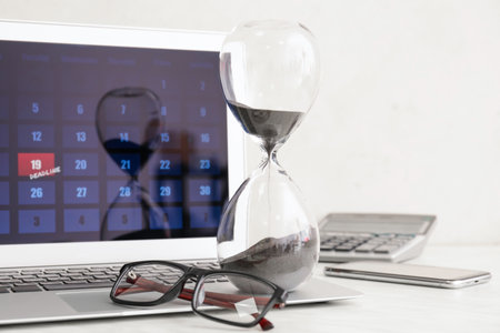 Hourglass, eyeglasses and laptop with calendar on light background. Dead line conceptの写真素材