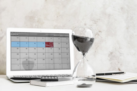 Hourglass and laptop with calendar on light table. Dead line concept