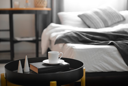 Cup of coffee with book and decor on table in bedroom, closeup