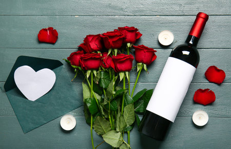 Bottle of wine, rose flowers, burning candles and envelope on green wooden background. Valentine's Day celebrationの写真素材