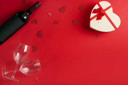 Bottle of wine, glasses, gift and hearts on red background. Valentine's Day Celebrationの写真素材