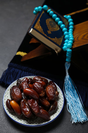 Plate of dates, prayer beads, Koran and mat for Ramadan on dark background
