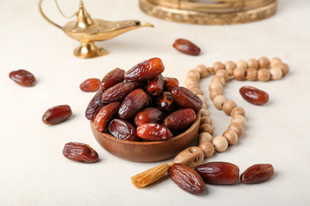 Bowl with dates, prayer beads and Muslim lamp for Ramadan on light background, closeup