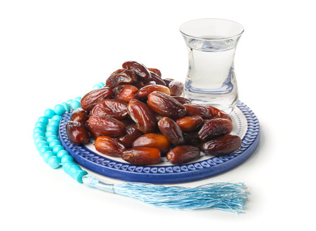 Plate with dried dates, glass of water and prayer beads for Ramadan on white backgroundの写真素材