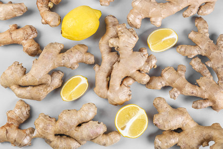 Fresh ginger roots and lemon on gray background, closeup