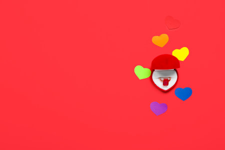 Engagement ring and hearts in colors of LGBT flag on red background. Valentine's Day celebration