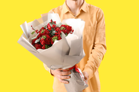 Young man with bouquet of flowers on yellow background, closeup. Valentine's Day celebrationの写真素材