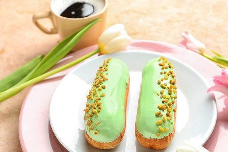 Plate with delicious eclairs and beautiful flowers on light background