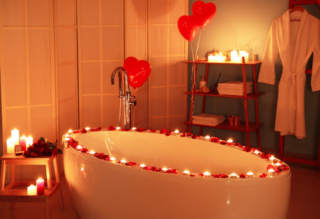 Interior of dark bathroom decorated for Valentine's Day with bathtub, burning candles and balloonsの写真素材