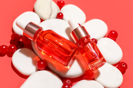 Composition with bottles of serum, spa stones and cranberry on red background, closeupの写真素材