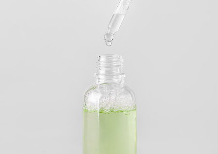 Dripping of serum from pipette into glass bottle on light background, closeup