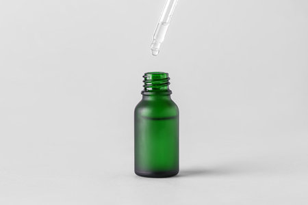Dripping of serum into green glass bottle on light backgroundの写真素材